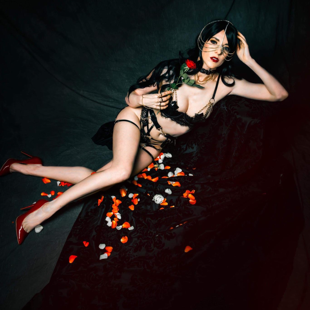 A person in black lingerie posing with rose petals on a dark surface.