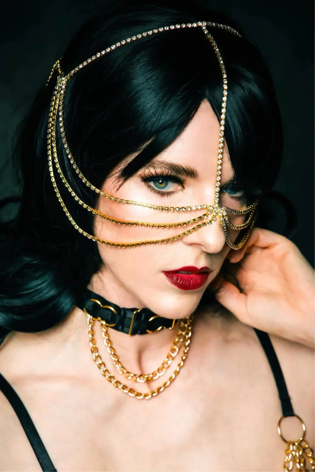 Striking portrait featuring dark hair, red lips, and decorative gold chain face jewelry.