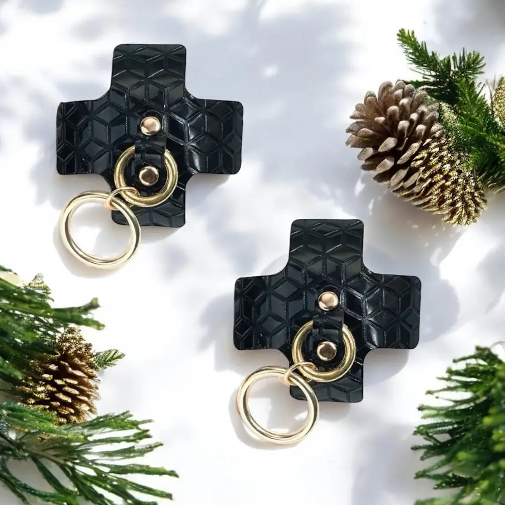 Black leather cross-shaped keychains with gold metal rings and hardware.