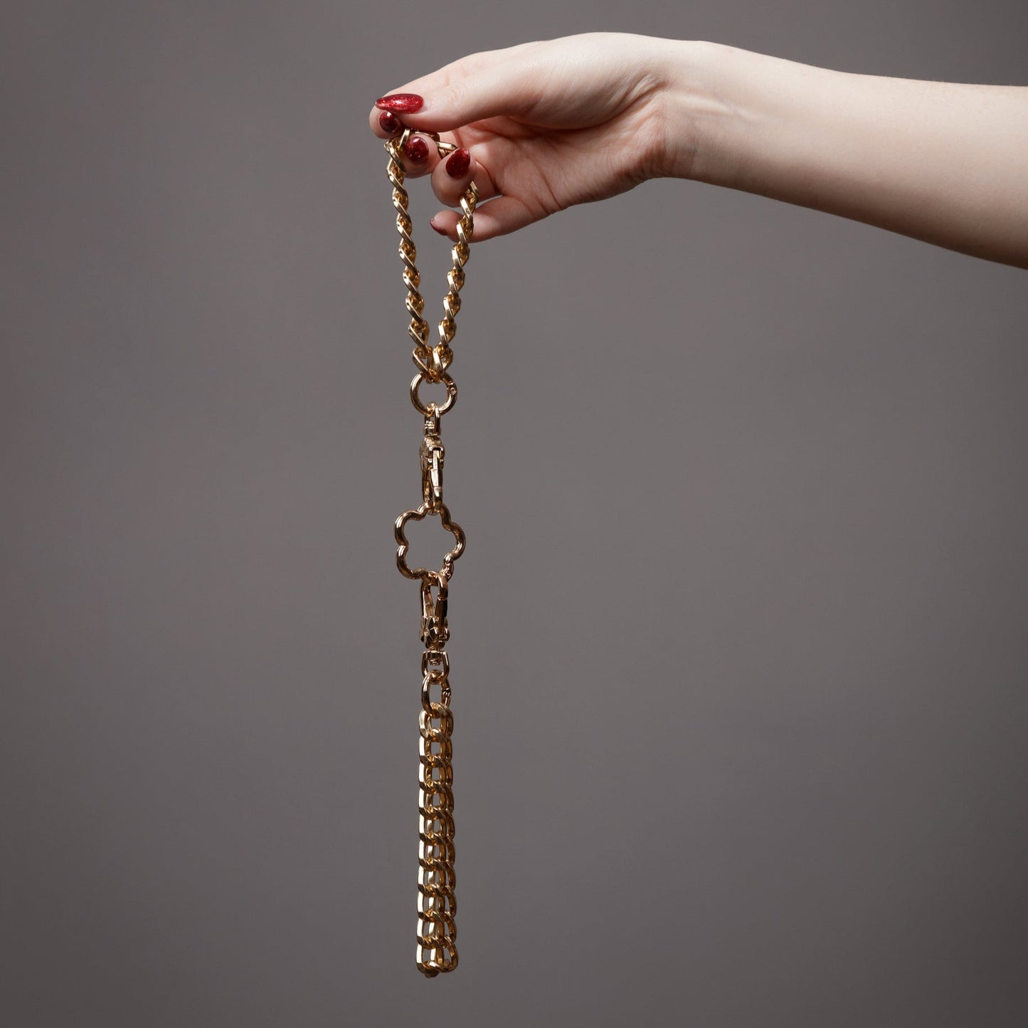 kinki couture Gold chain handcuffs held by a hand against a gray background
