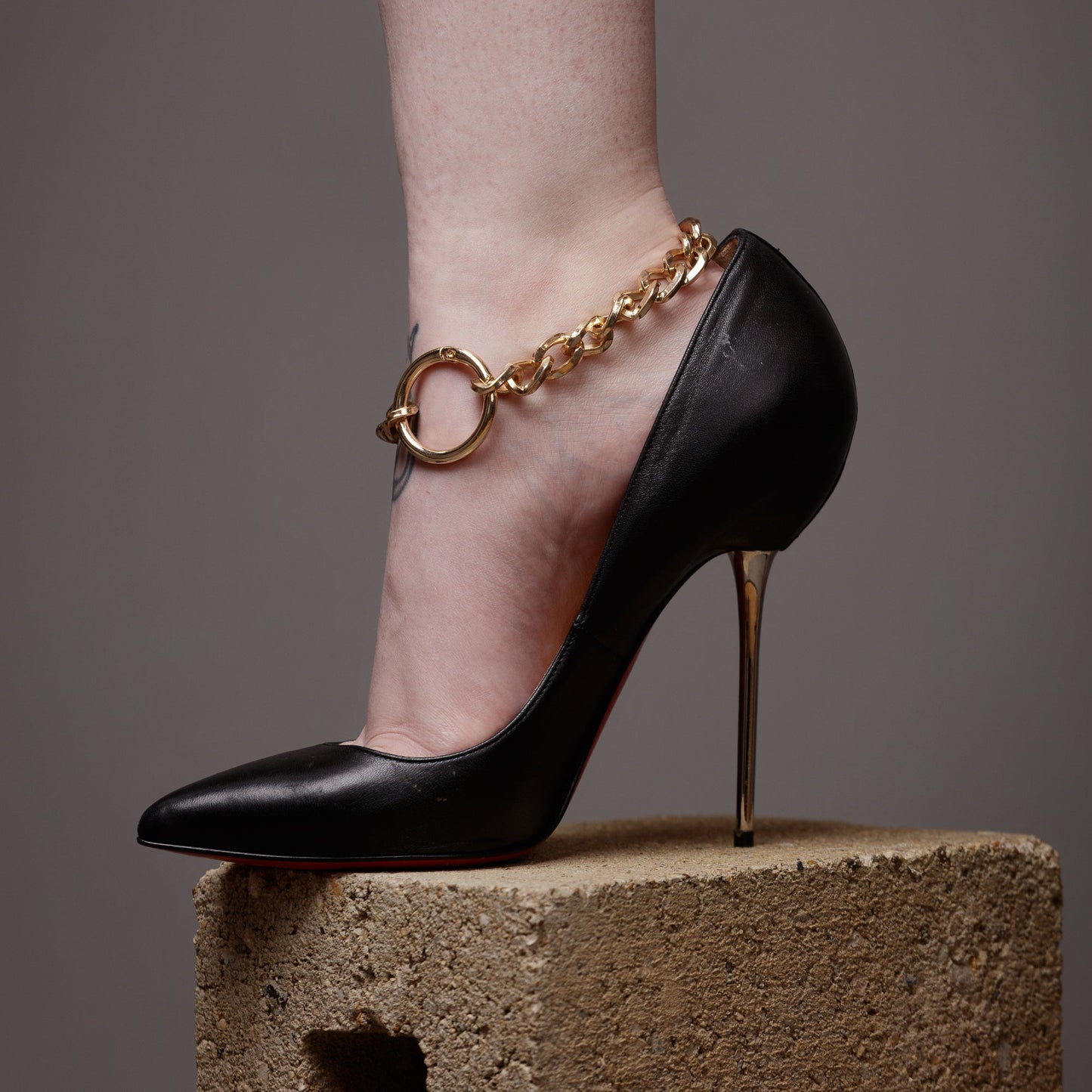 Black high-heeled shoe with a gold bdsm ankle cuffs on a neutral background