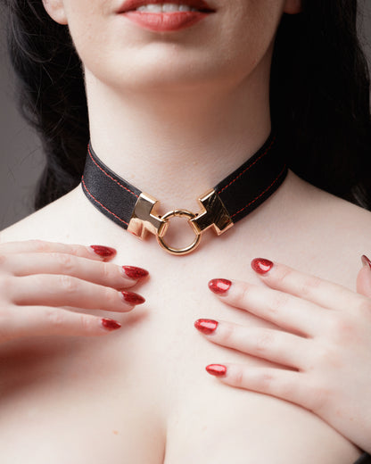Close-up of a woman wearing a black and gold o-ring bondage choker with a gold clasp.