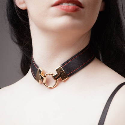 Close-up of a person wearing a black choker with gold clasp on a neutral background