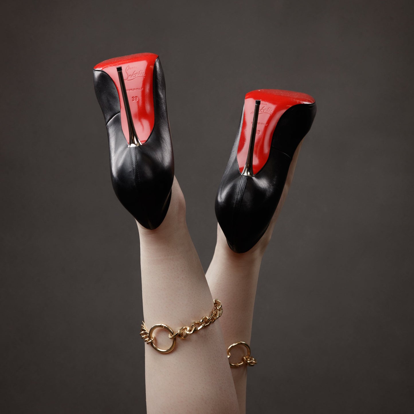Black high-heeled shoes with red soles and gold ankle cuffs