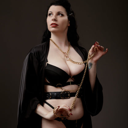 Woman wearing a black outfit with gold chain collar and leash against a dark background