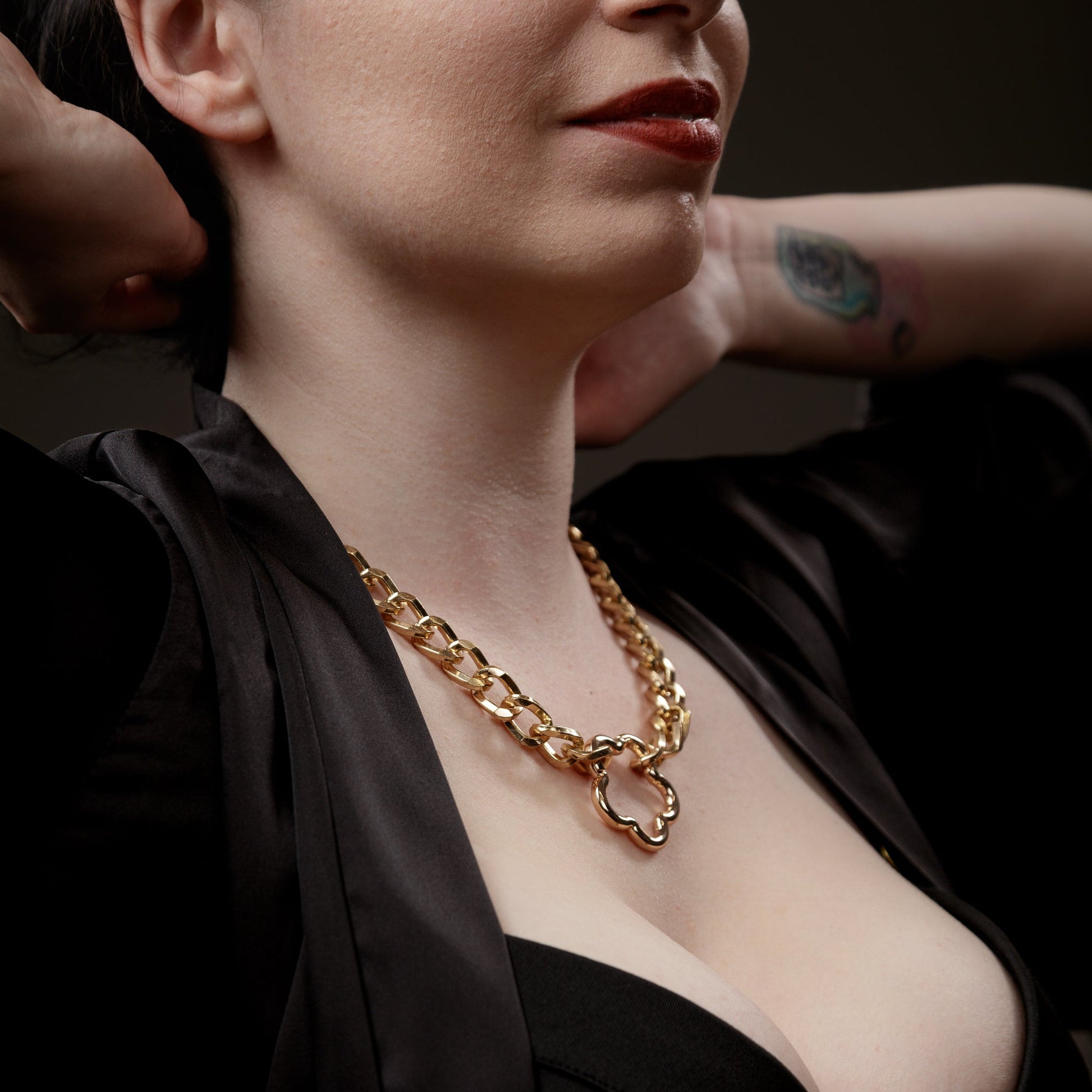Woman wearing a gold chain bdsm kinkwear necklace with a dark background